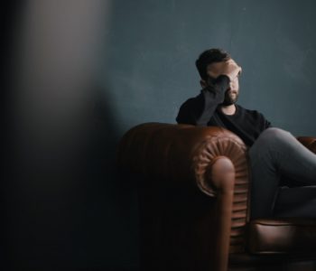 a man holds his head while sitting on a sofa