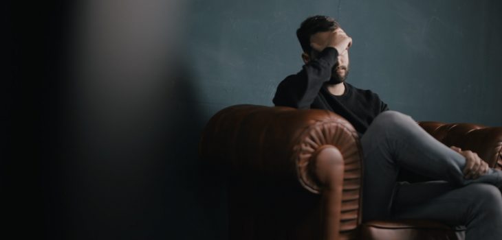 a man holds his head while sitting on a sofa