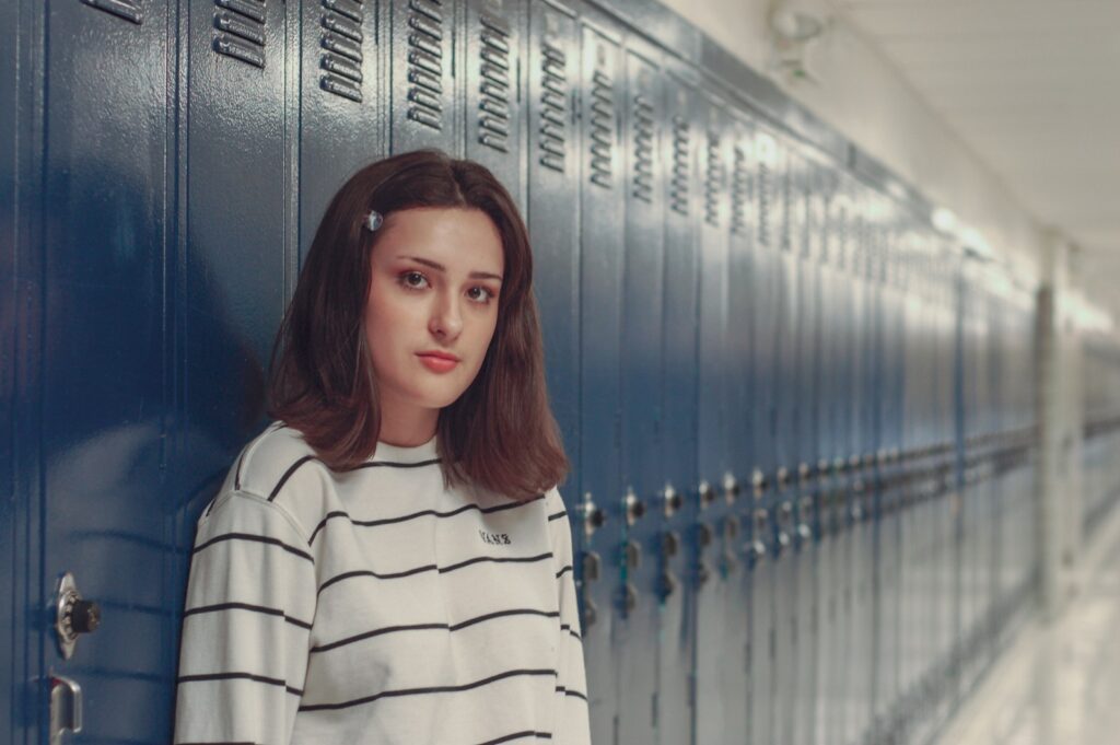 Teen feeling nervous about back-to-school social anxiety standing by school lockers.