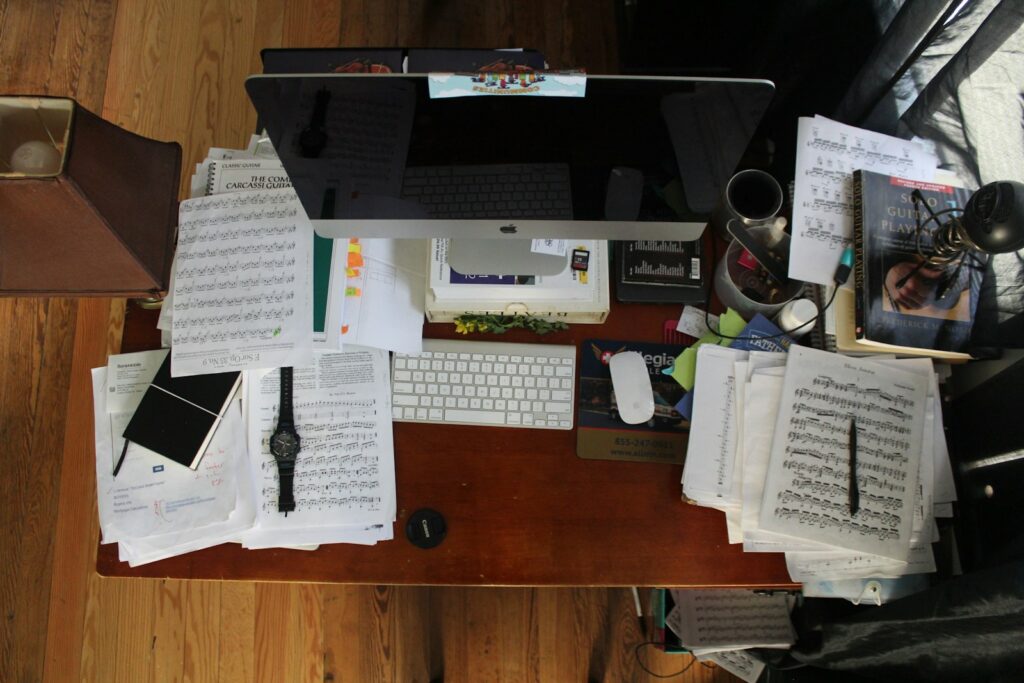 Messy desk covered with scattered papers, notebooks, and office supplies.