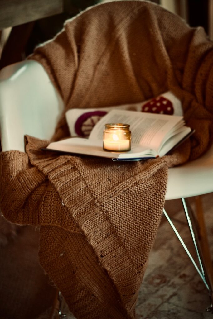 Candle, warm blanket, and autumn leaves creating a cozy fall atmosphere.