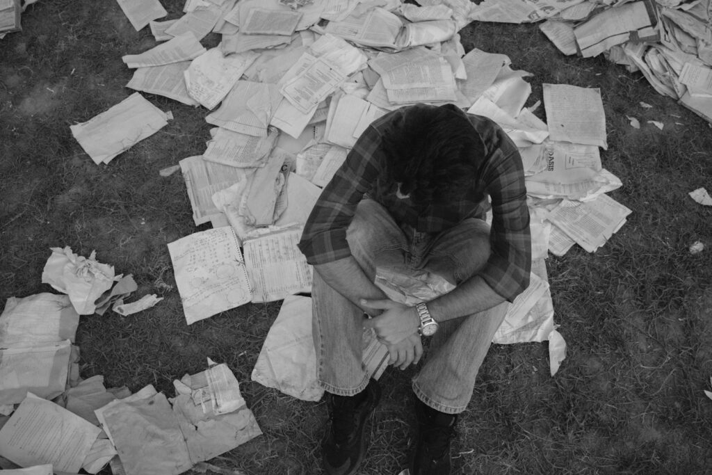 Person sitting on the floor surrounded by scattered papers, symbolizing the exhaustion and overwhelm of perfectionism.