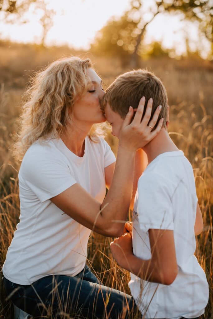 Mother holding her son's face gently and kissing his forehead outdoors in fall, symbolizing comfort and support for anxious kids during Halloween.