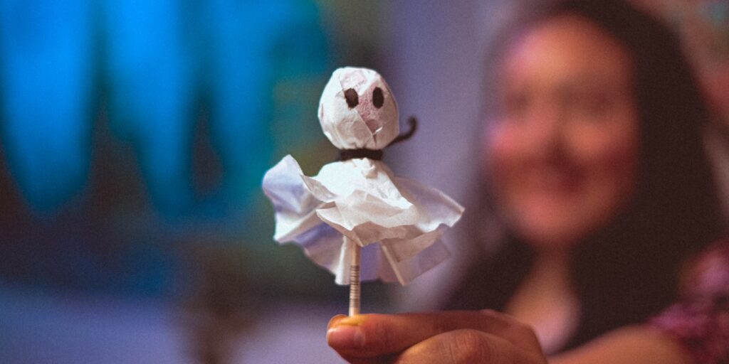 Adult's hand holding a small handmade ghost decoration made from crafting materials, representing gentle, creative ways to support anxious kids during Halloween.