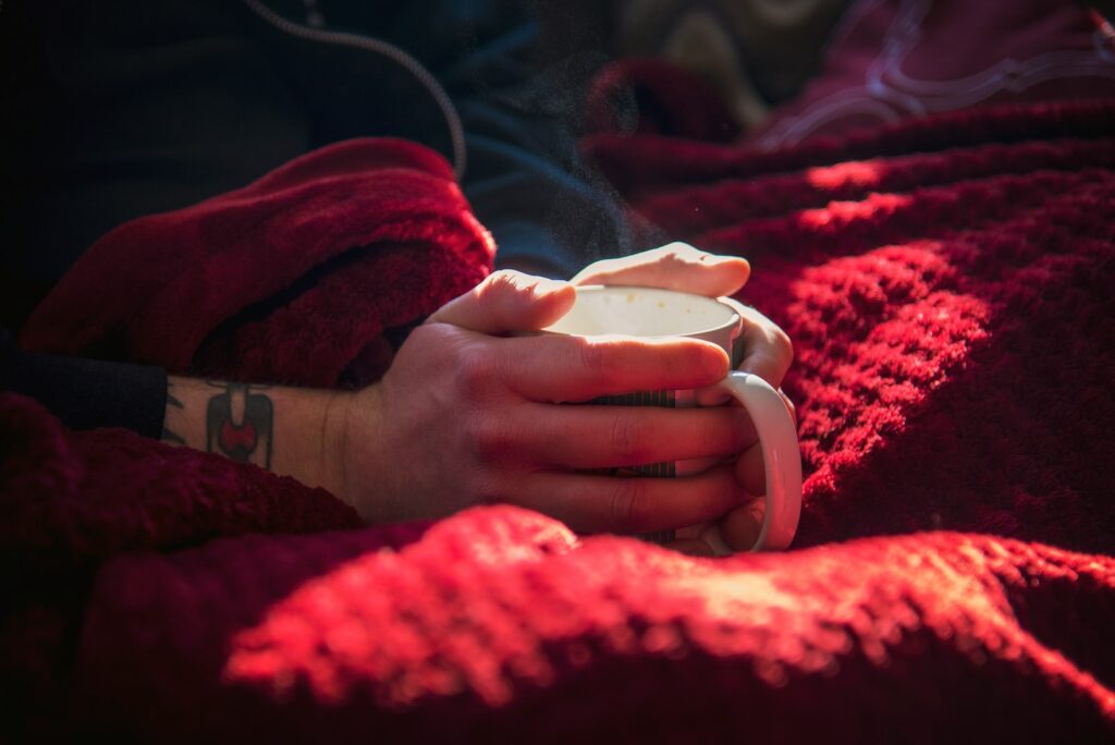 a person holding a mug while resting on a blanket