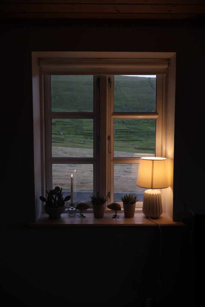 A softly lit lamp and candle in a window at dusk