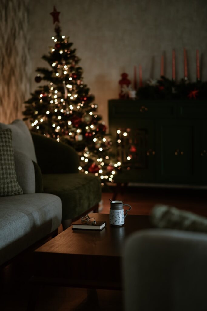 A dimly lit living room with a couch, coffee table, and mug, and a holiday tree lit in the background