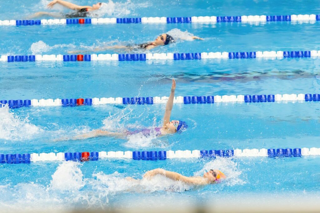 Four young swimmers mid-backstroke, illustrating focus, effort, and sports anxiety in kids under performance pressure