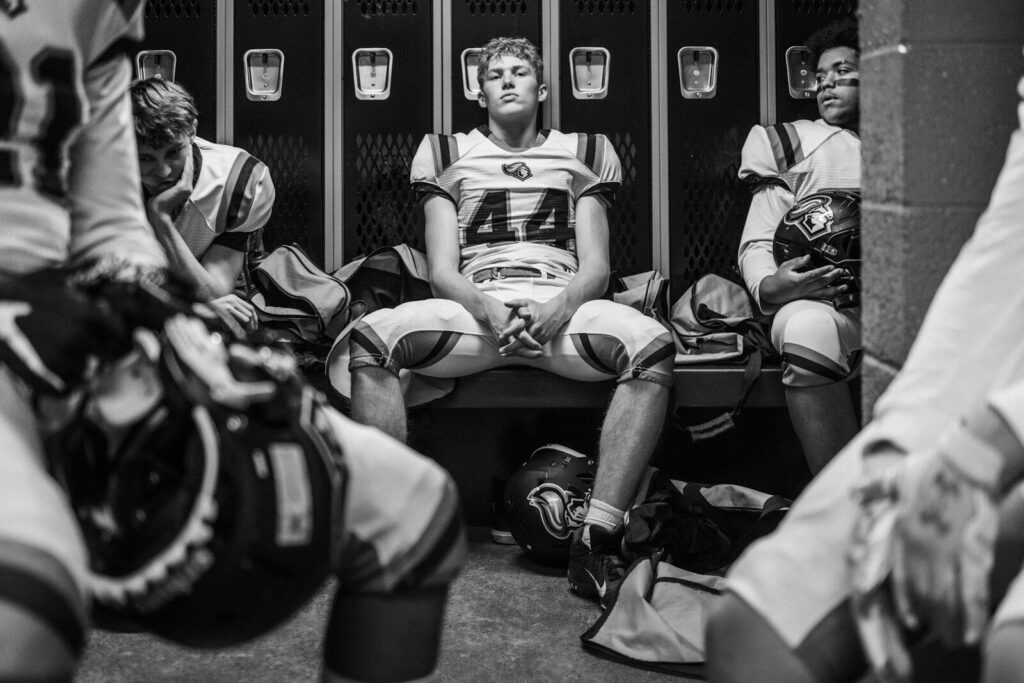 Teen football players sitting in locker room, reflecting on sports performance and pressure.