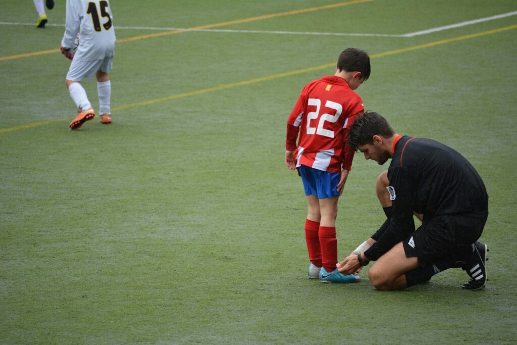 Adult assisting a child soccer player with tying cleats, symbolizing support and guidance in youth sports