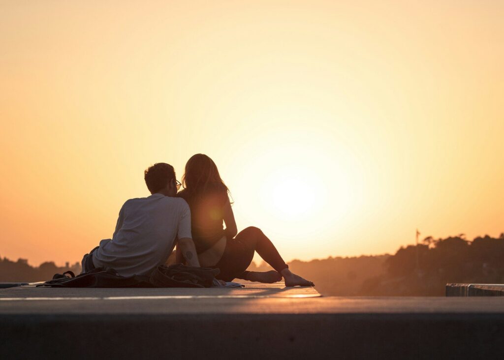 Couple sitting together facing a sunset, viewed from behind, symbolizing connection and hope after overcoming relationship anxiety.