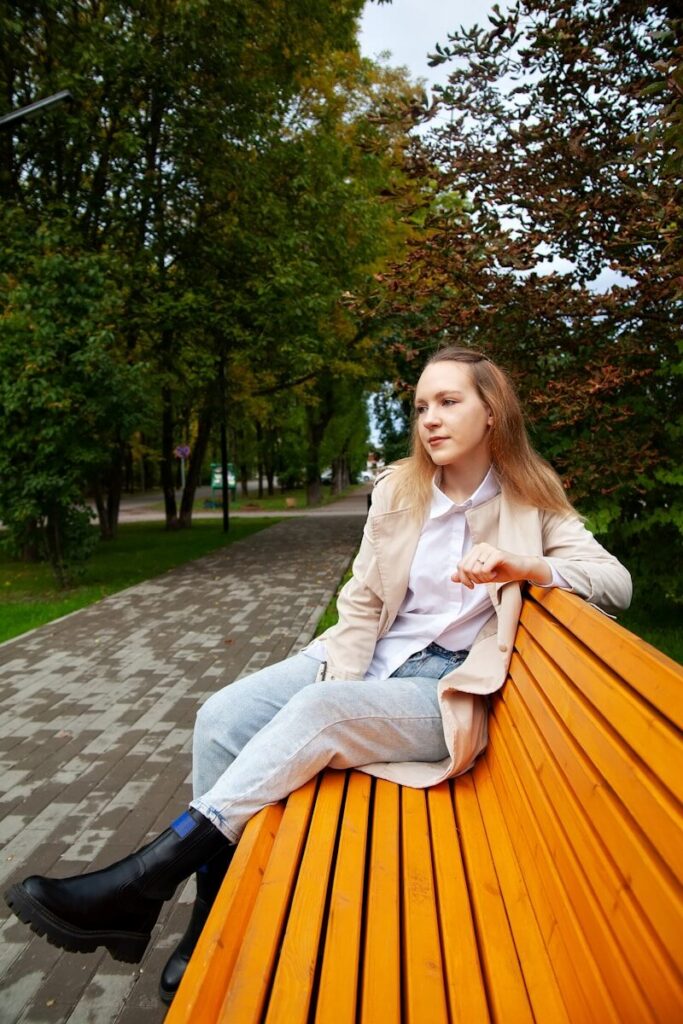 Woman sitting on a park bench, looking thoughtfully into the distance with trees in the background, reflecting on her thoughts.
