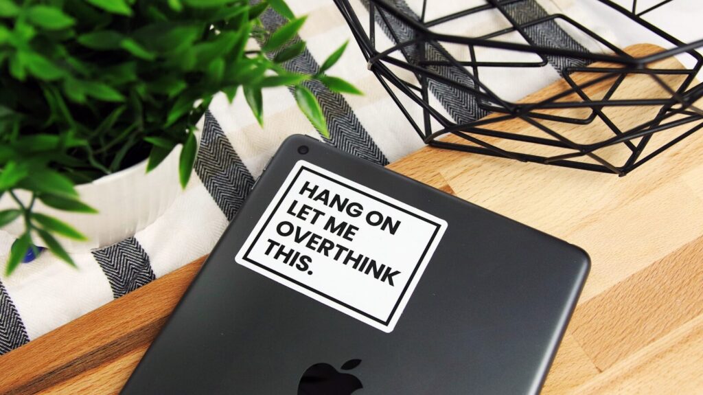 Laptop on a desk with a sticker reading "Hang on let me overthink this" representing chronic worry and overthinking in generalized anxiety disorder